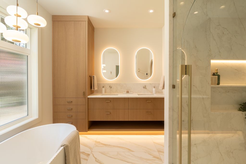 Primary ensuite with oak vanity, backlit mirrors and marble tile