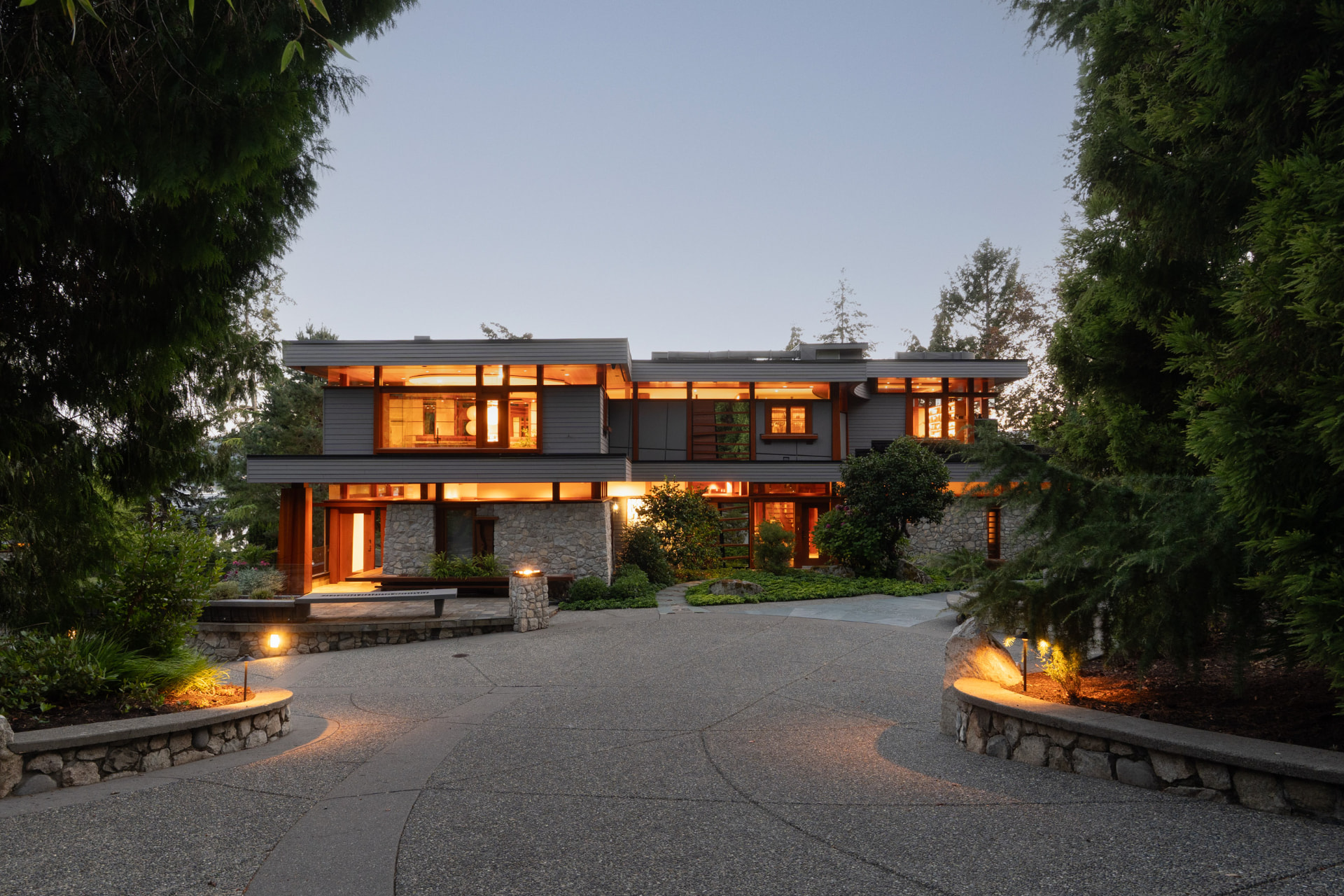 West Coast contemporary residence glowing at dusk framed by cedars